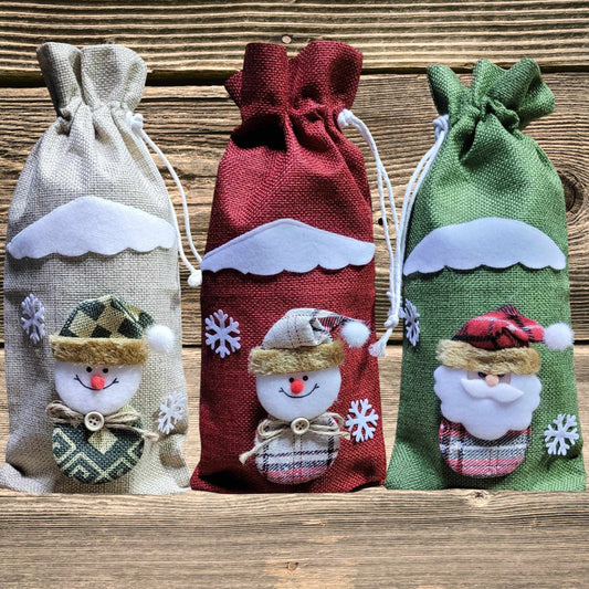 Three tall burlap gift bags with festive snowman and Santa designs, perfect for wrapping goat milk soap sets for holiday gifting.