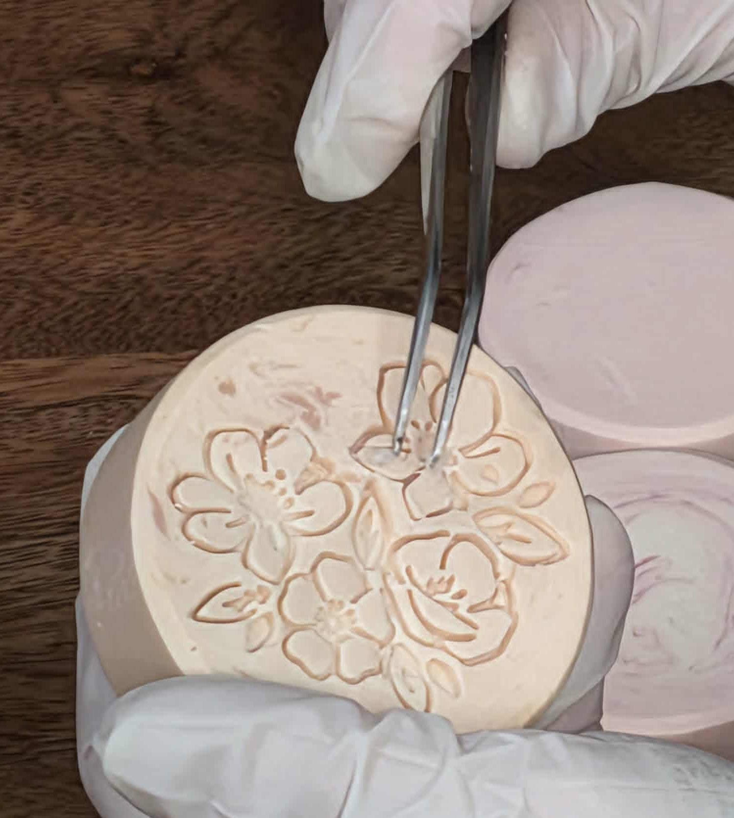 Close-up of fine-tipped tweezers removing residue from a stamped floral soap design before mica painting.