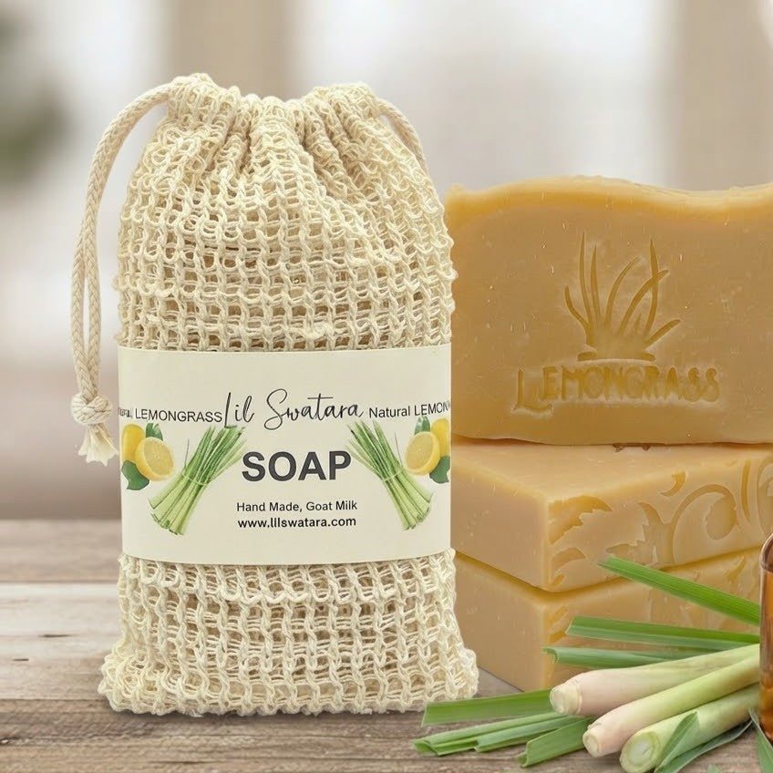 Natural Lemongrass goat milk tallow soap bars displayed with fresh lemongrass stalks, an amber glass bottle, and a labeled drawstring soap bag on a wooden surface.
