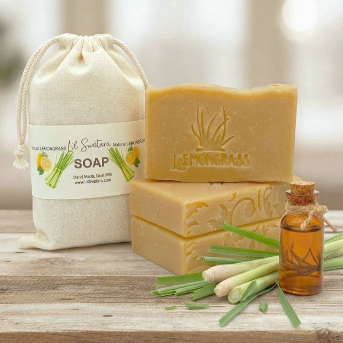 Natural Lemongrass goat milk tallow soap bars stacked beside a drawstring bag labeled Natural Lemongrass, with fresh lemongrass stalks on a wooden surface.
