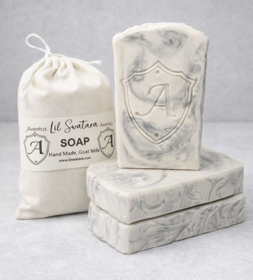 Aventus tallow goat milk soap with steel‑grey marbling and shield emboss beside branded muslin bag, creamy birch musk scent, handmade by Lil Swatara.