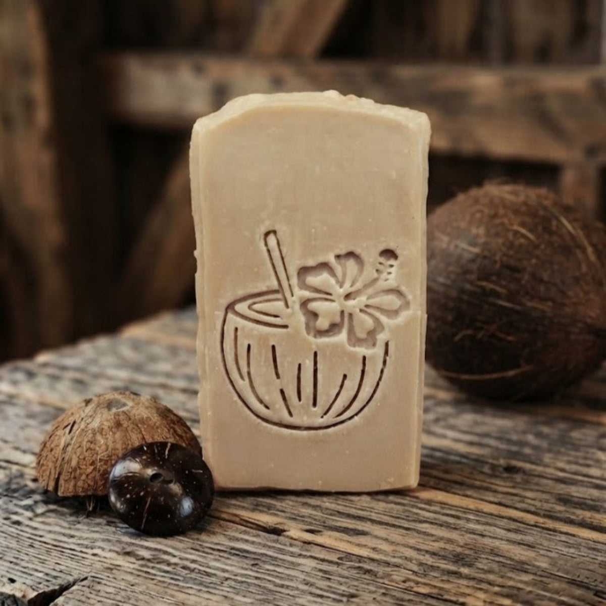 Black Coconut goat milk soap bar with engraved coconut drink design on rustic barnwood beside coconut shell pieces and a whole coconut.
