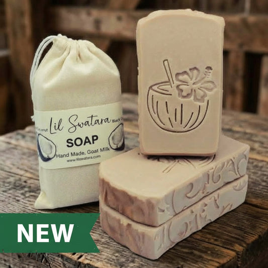 Black Coconut goat milk soap bar with engraved coconut drink design, shown beside its muslin sack packaging on rustic barnwood, handmade tallow blend XL 6oz bar.
