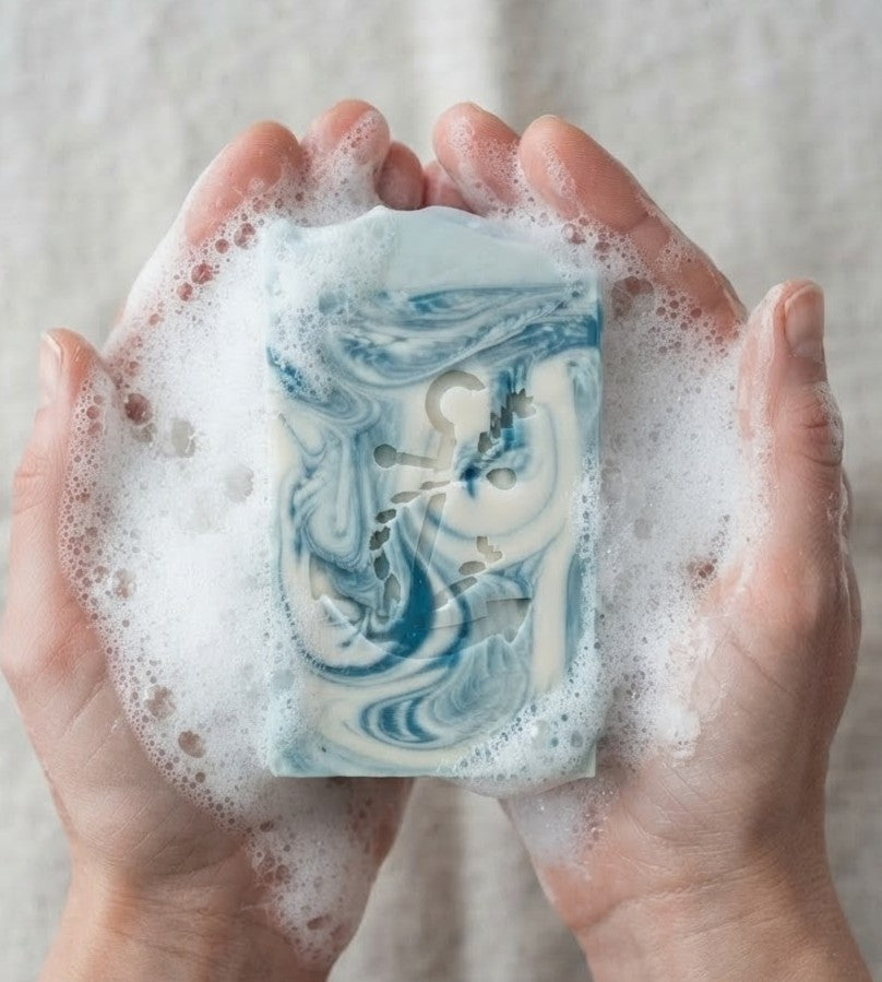 Bleu Coastal Musk tallow goat milk soap held in lathered hands with blue‑white marbling and anchor emboss, handmade by Lil Swatara.