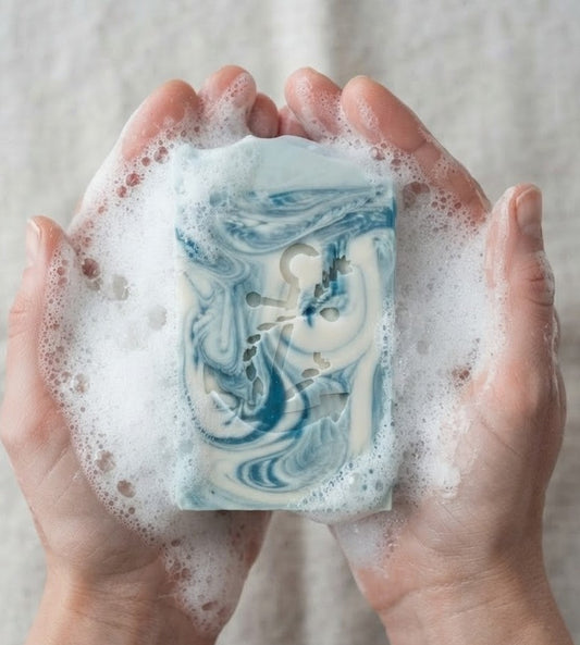 Bleu Coastal Musk tallow goat milk soap held in lathered hands with blue‑white marbling and anchor emboss, handmade by Lil Swatara.