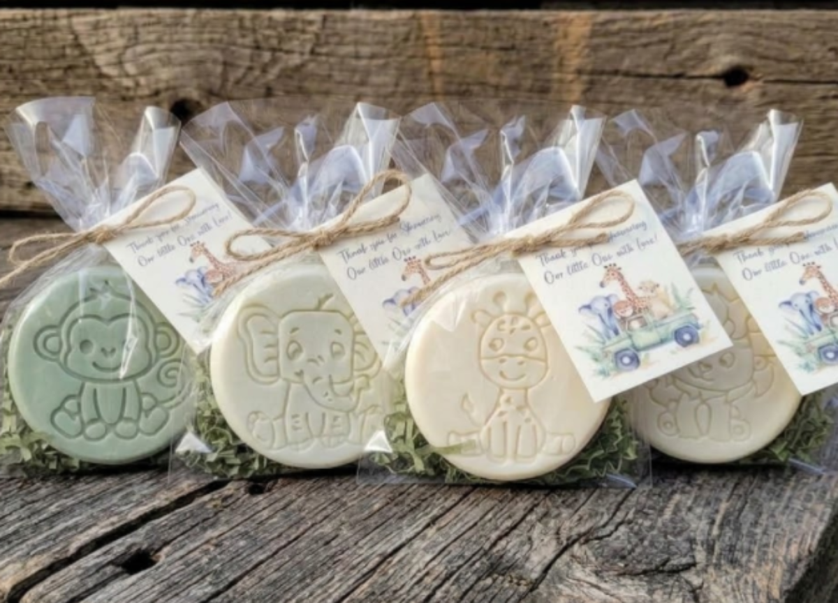 Four safari-themed soap stamped baby shower soap favors wrapped in clear cellophane bags with twine and printed tags, displayed on a rustic wooden surface.