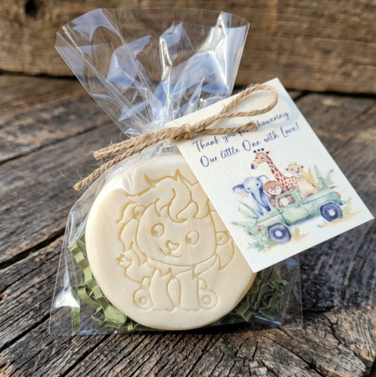 Handcrafted cream-colored lion-embossed goat milk soap packaged in a clear cello bag with green crinkle shred, tied with a jute twine bow and a watercolor safari baby shower thank you tag.