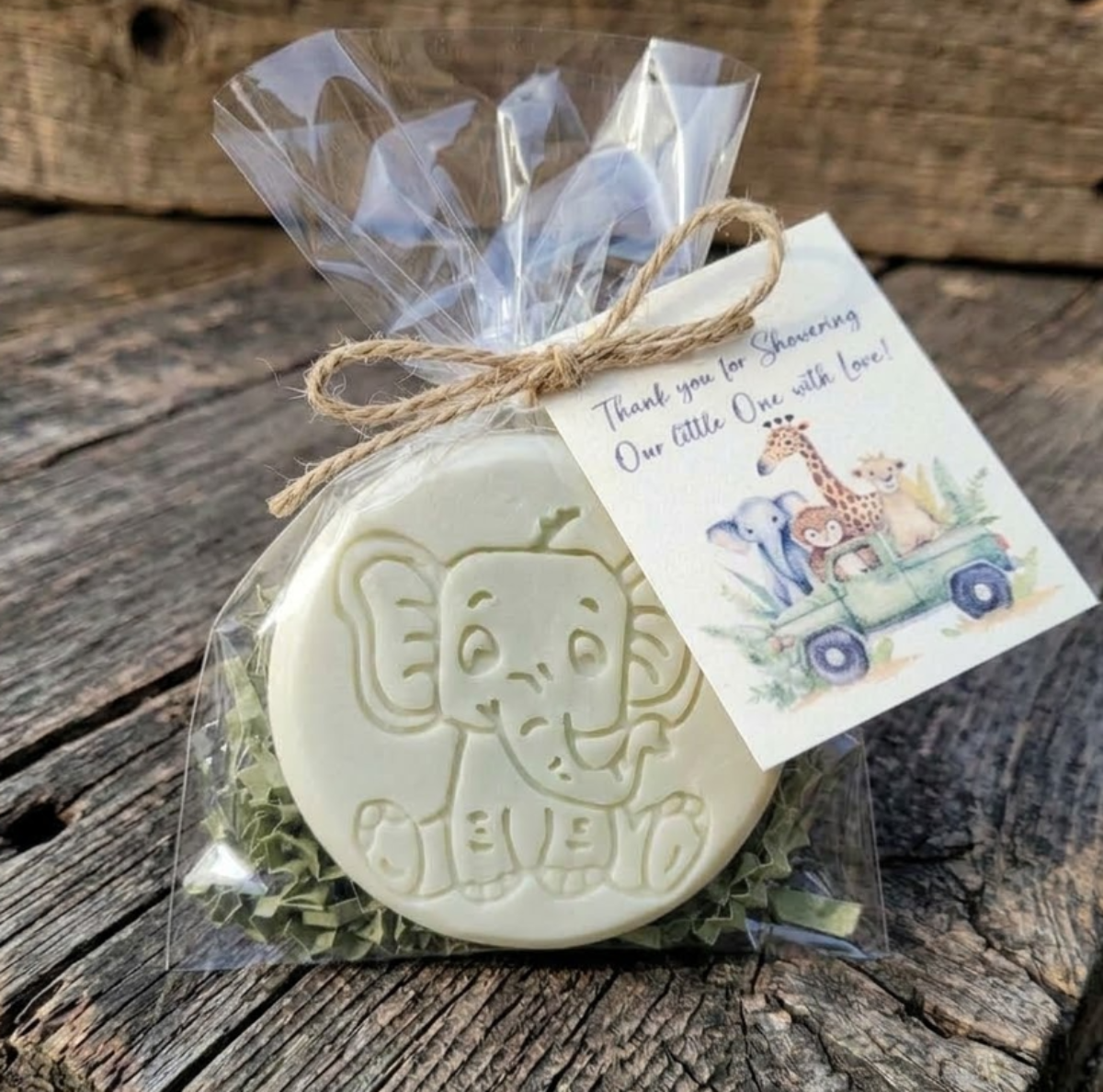 Handcrafted cream-colored elephant-embossed goat milk soap packaged in a clear cello bag with green crinkle shred, tied with a jute twine bow and a watercolor safari baby shower thank you tag.