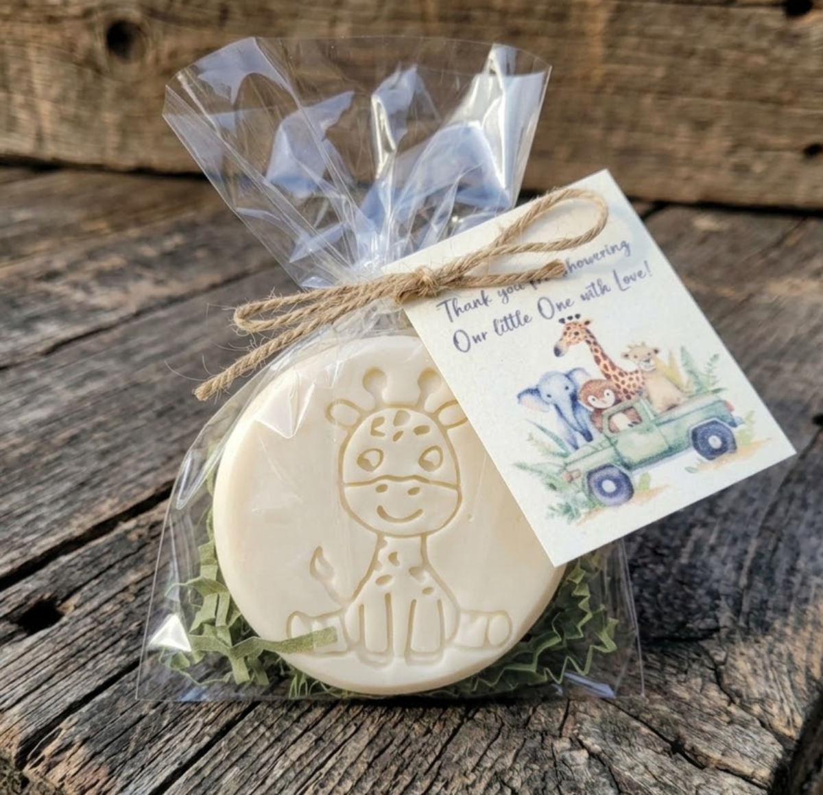 Handcrafted cream-colored giraffe-embossed goat milk soap packaged in a clear cello bag with green crinkle shred, tied with a jute twine bow and a watercolor safari baby shower thank you tag