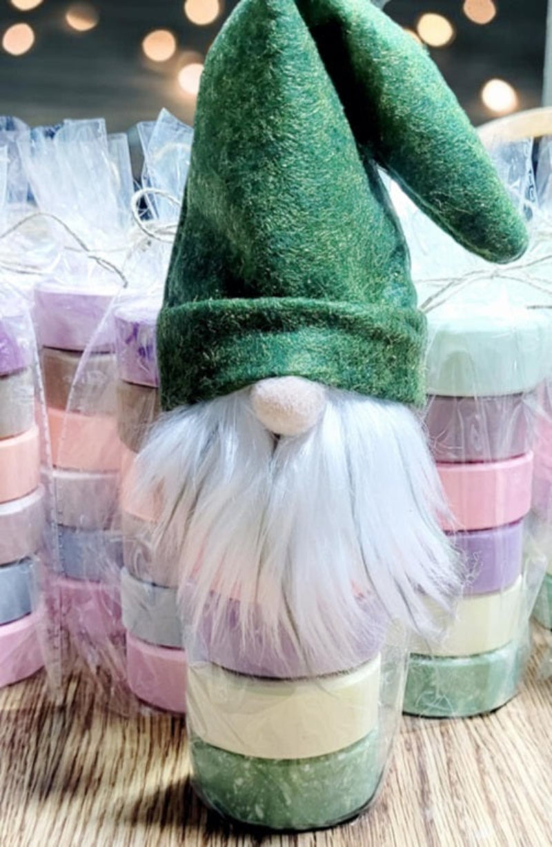 Whimsical gnome hat wraps with stacked pastel soap pucks, packaged in clear bags with red, green, and gray hats for festive gifting.