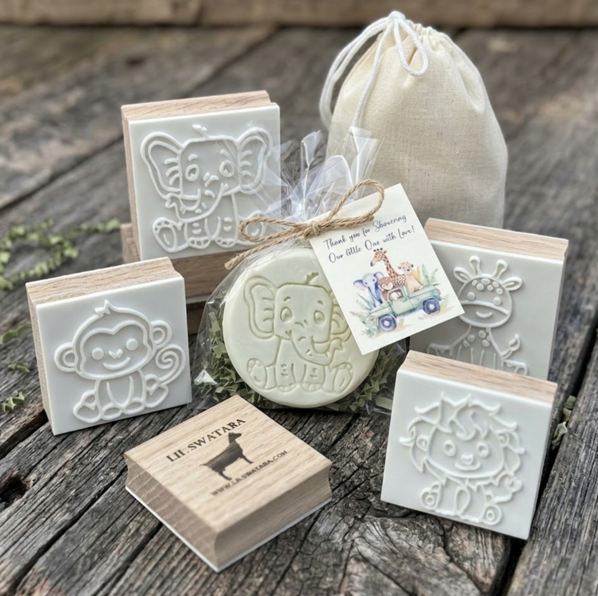 set of four jungle safari animal favor soaps (monkey, elephant, giraffe, lion) individually packaged in clear bags with jute twine and baby shower gift tags, arranged in a row on a rustic wooden background.