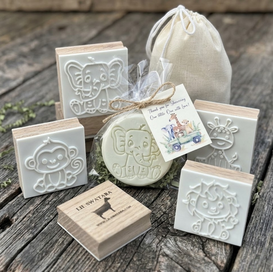 set of four jungle safari animal favor soaps (monkey, elephant, giraffe, lion) individually packaged in clear bags with jute twine and baby shower gift tags, arranged in a row on a rustic wooden background.