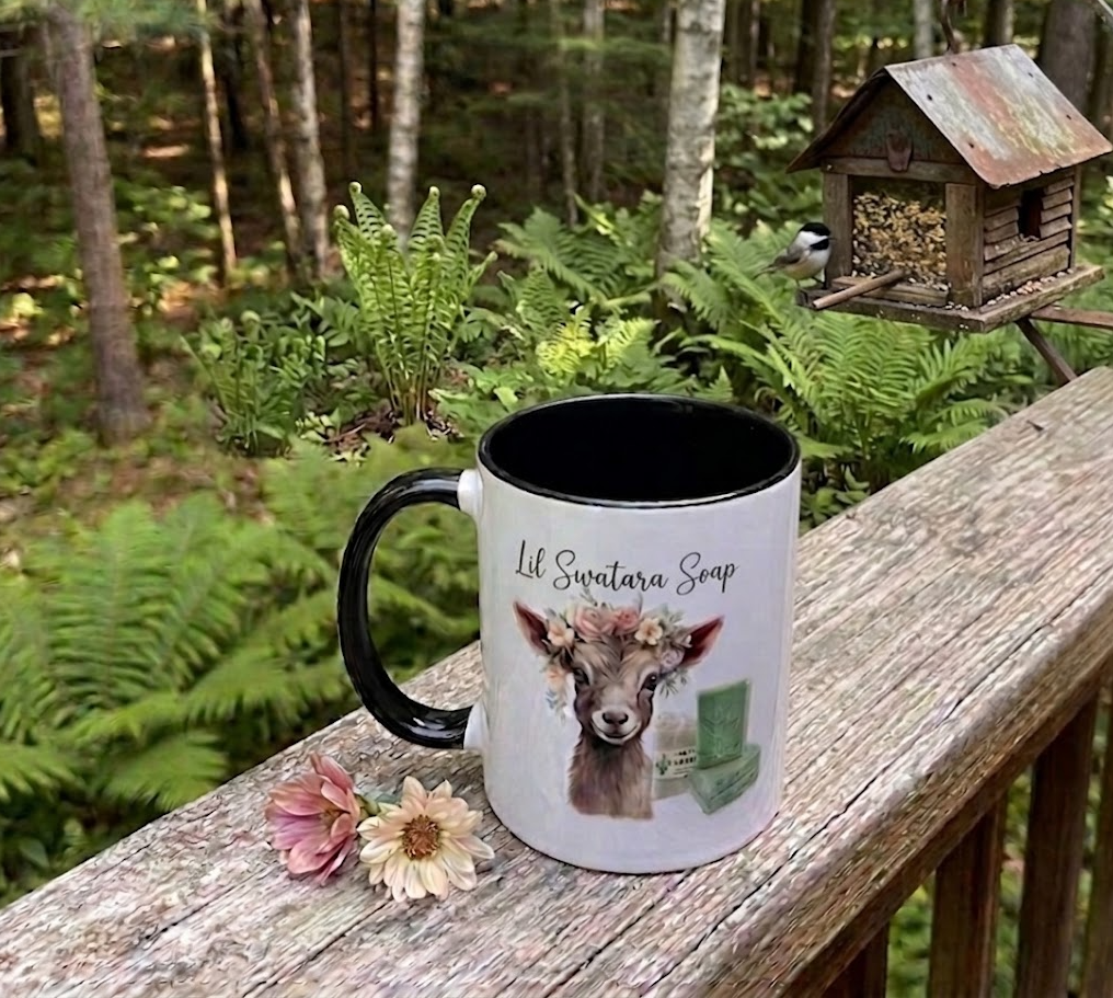 Lil Swatara Soap goat mug with black accents displayed outdoors with flowers in a forest setting
