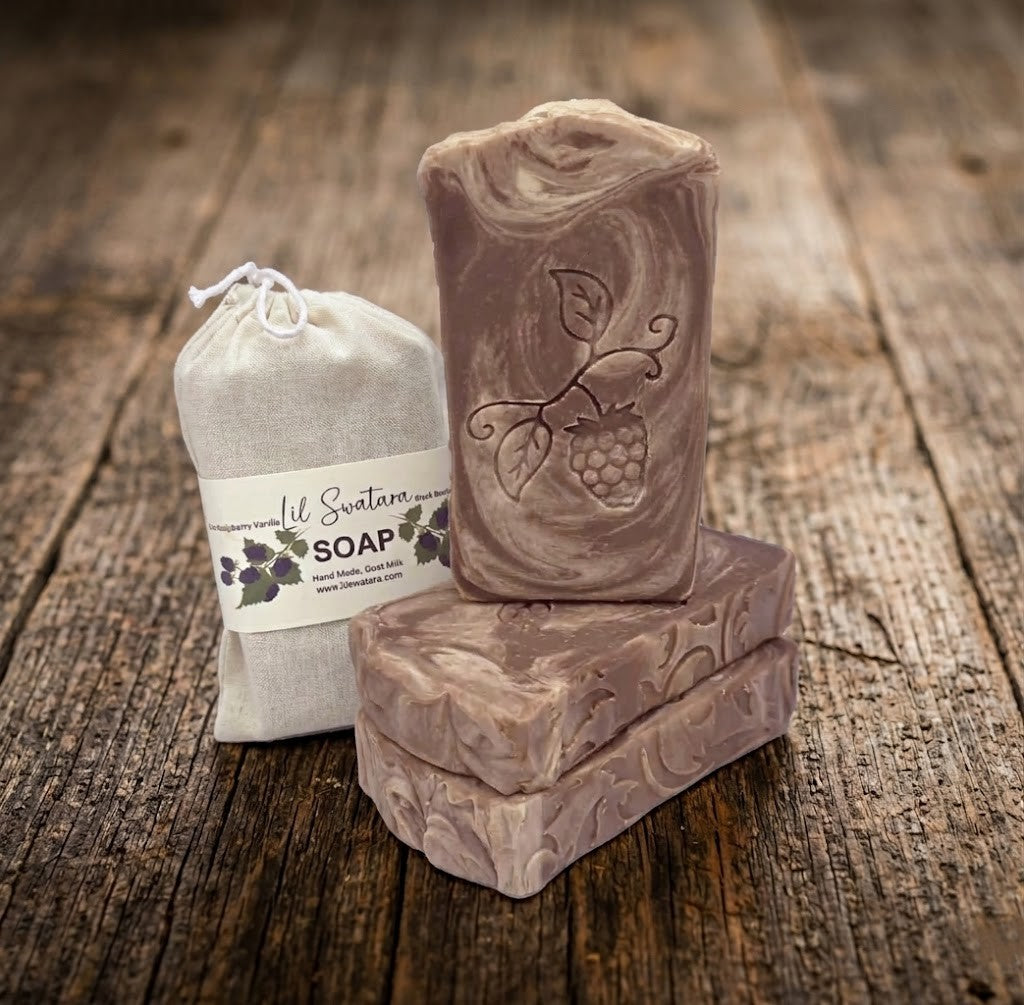 Handmade goat milk and tallow soap bar with embossed raspberry design next to a cotton drawstring bag on a rustic wood surface