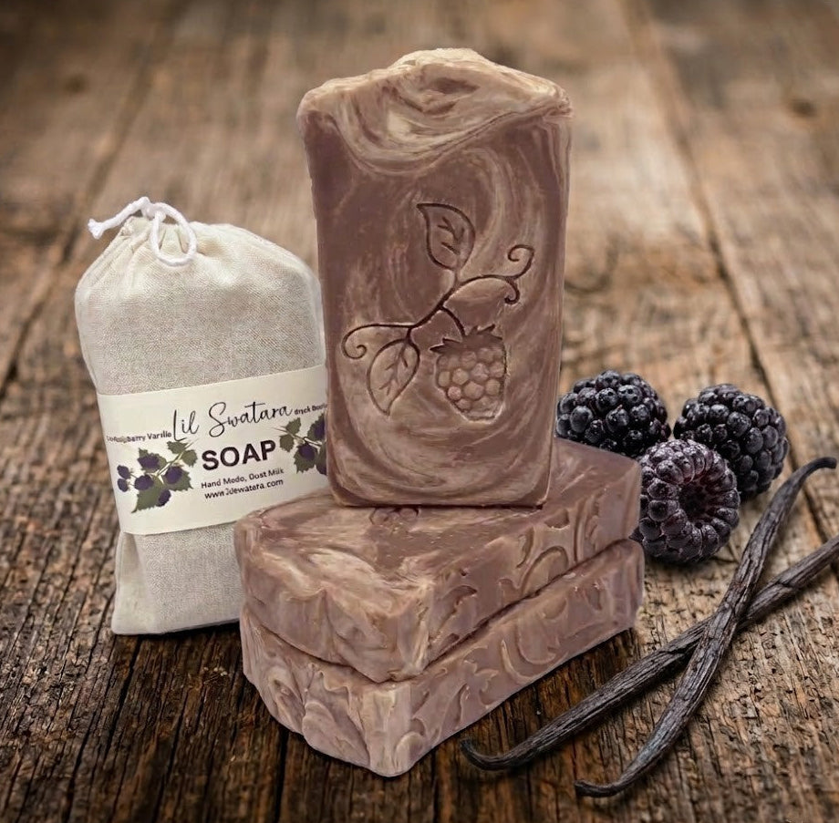 Handmade goat milk and tallow soap bar with embossed raspberry design next to a cotton drawstring bag on a rustic wood surface