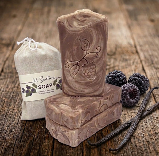 Handmade goat milk and tallow soap bar with embossed raspberry design next to a cotton drawstring bag on a rustic wood surface