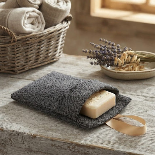 Handmade Oats, Milk & Honey soap tucked inside a grey textured exfoliating soap bag with a satin ribbon loop, displayed in a rustic country setting.