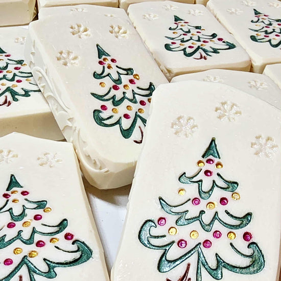 Hand-painted goat milk soap bar with festive Christmas tree design, wrapped in clear packaging with goat tag for holiday gifting