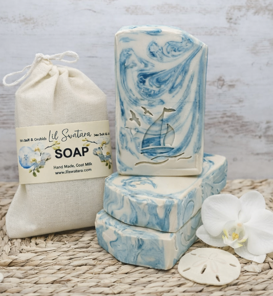 Sea Salt & Orchid tallow goat milk soap with creamy white base and teal swirls, sailboat stamp, orchid flower, and sand dollars on soft coastal beach with dunes and pale sky.
