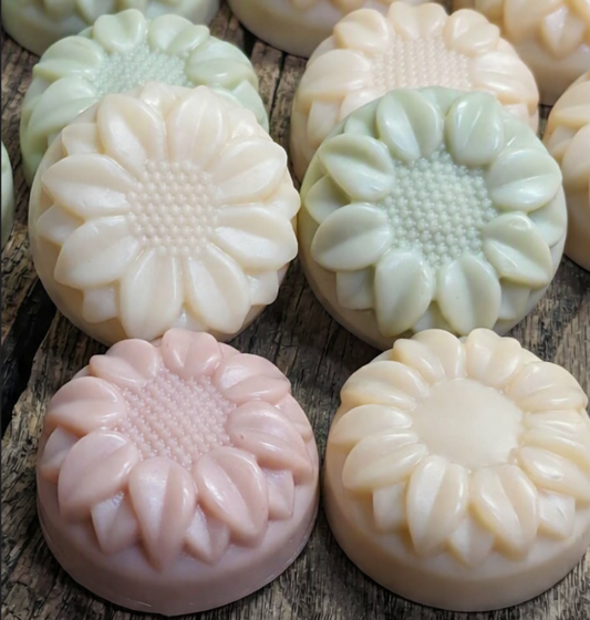 Handcrafted tallow shampoo flower bars in assorted colors on wood background.