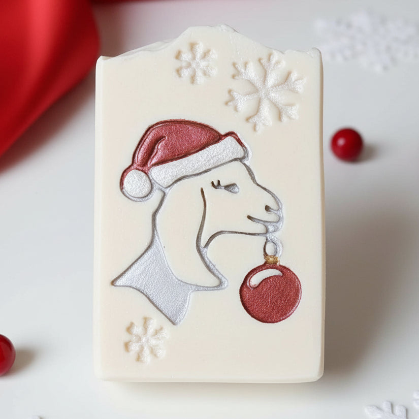A close-up of multiple rectangular white soaps arranged in rows, each decorated with an embossed goat wearing a red Santa hat and holding a red ornament, with white snowflake details.