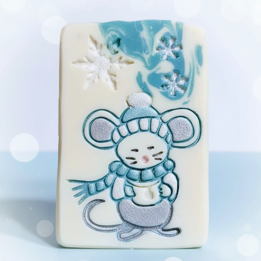 Soap stamp of a cute winter Christmas mouse drinking hot chocolate from a mug stamped on pretty goat milk soap.