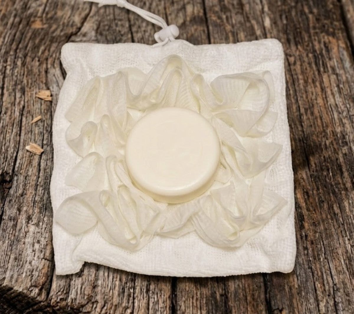 Dual‑sided soft wash ball with round goat milk soap puck inside a reversible drawstring pouch, shown on rustic wood for Lil Swatara Soap.