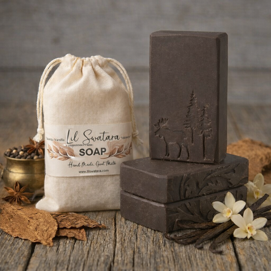 Handcrafted Tobacco Vanilla goat milk tallow soap bars stacked beside a muslin drawstring bag labeled Lil Swatara Soap, surrounded by dried tobacco leaves, vanilla beans, and cream‑colored vanilla flowers on a rustic wooden surface.