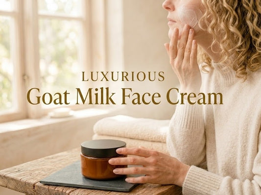 A blonde woman with curly hair applying a rich layer of unscented goat milk face cream to her cheek, sitting next to a jar of the moisturizer.